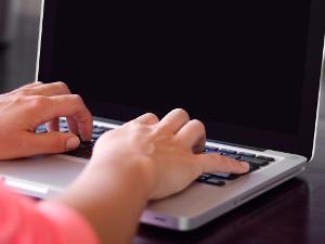 Ein Mensch sitzt an einem Laptop hat hat die Hände auf der Tastatur liegen, der Monitor ist schwarz