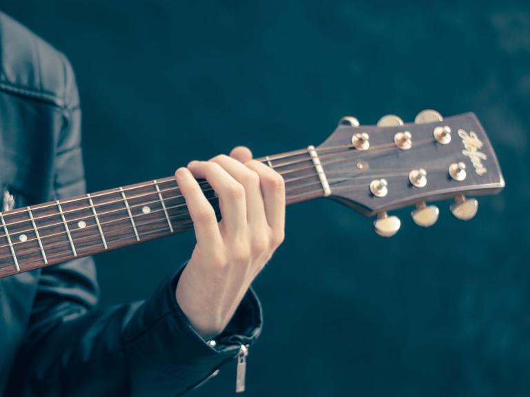 Eine Person hat eine Gitarre in der Hand, man sieht den Gitarrenhals mit einer Hand daran