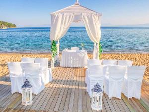 Stühle mit weißen Stuhlhussen und Laternen auf einem Holzboden am Strand