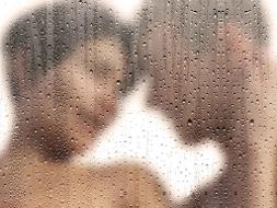 Mann und Frau haben die Köpfe aneinanderliegend und sind verschwommen hinter einer Glasscheibe mit Regentropfen zu sehen