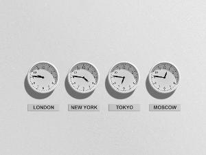 Vier weiße Uhren nebeneinander zeigen verschiedene Uhrzeiten an- darunter London, New York, Tokyo und Moscow auf einem Schild stehend