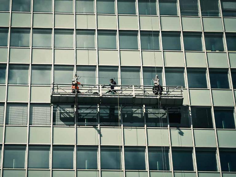 Drei Männer auf einer Plattform die an Seilen an einer Gebäudefassade hängt