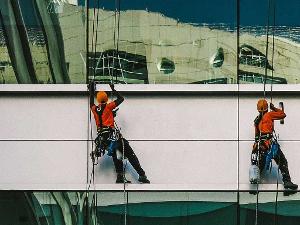 Zwei Männer hängen an Seilen an einer Gebäudefassade und reinigen diese