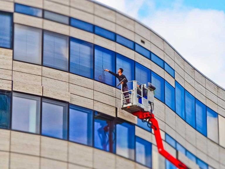 Ein Mann steht auf einer Plattform und reinigt die Fenster eines Gebäudes