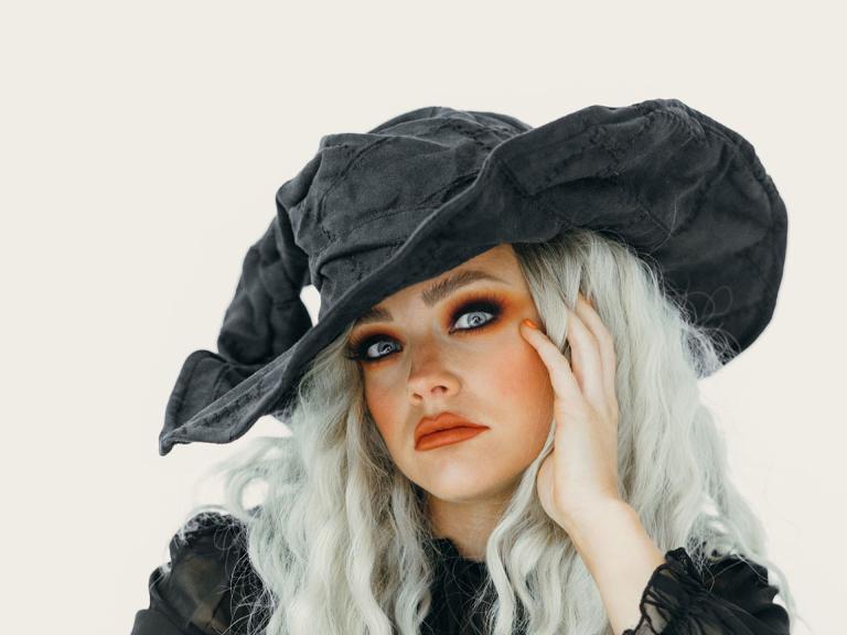 Eine Frau mit einem großen schwarzen Hut und kräftigem Makeup, verkleidet als Hexe