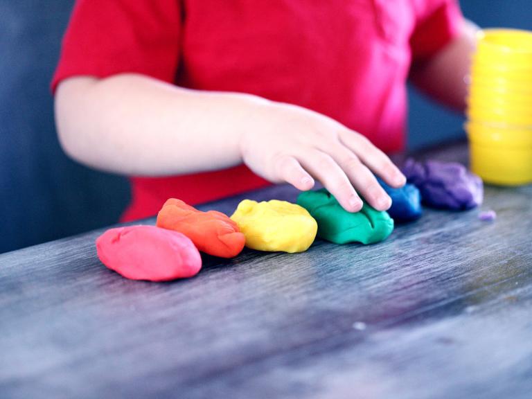 Sechs verschiedenfarbige Knetenhaufen liegen vor einem Kind auf dem Tisch