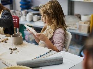 Ein Kind sitzt an einem Tisch und hat Keramikrohmasse vor sich liegen