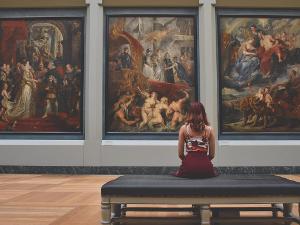 Eine Frau sitzt auf einer Bank vor drei großen Gemälden