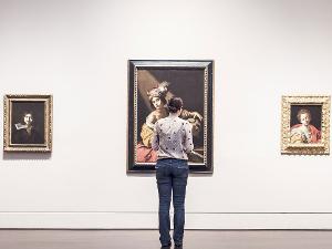 Eine Frau steht vor drei Bildern die an einer weißen Wand hängen