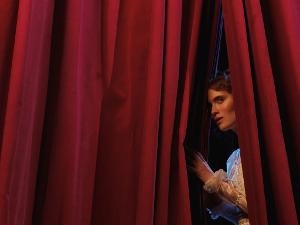 Eine Frau schaut durch einen roten Vorhang
