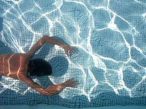 Eine Person schwimmt unter Wasser in einem Becken- Aufnahme von oben auf das Wasser