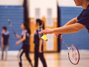 Eine Person hält einen Badmintonschläger in der einen und einen Federball in der anderen Hand- bereit für den Aufschlag