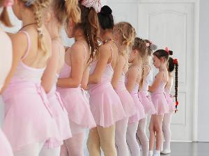 Mädchen stehen in rosafarbener Ballettkleidung mit dem Gesicht zur Ballettstange