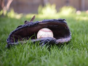 Ein Baseball liegt in einem Handschuh der auf dem Rasen liegt