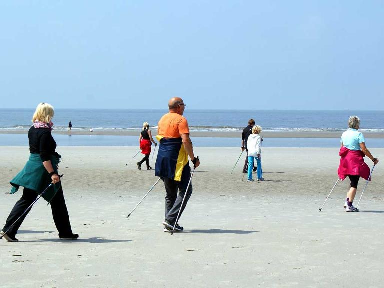 Menschen gehen auf dem Strand mit ihren Gehstöcken am Wasser entlang