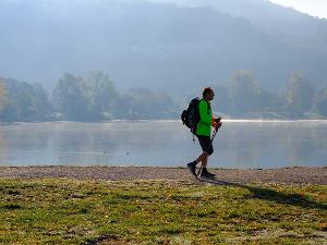 Ein Mann wandert auf einem Weg an einem See entlang, mit Gehstöcken in der Hand