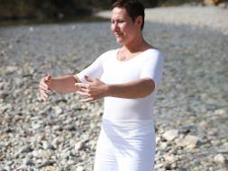 Eine Frau in weißer Kleidung macht eine Qigong Übung
