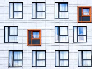 Zwölf Fenster mit schwarzem Rahmen an einer weißen Hauswand- bei zwei Fenstern ist der Rahmen orange