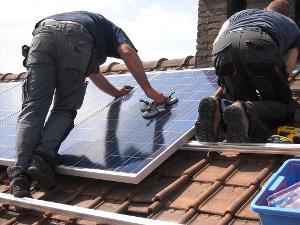 Zwei Menschen installieren auf dem Dach eine Solaranlage