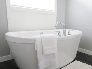 Eine freistehende weiße Badewanne- über dem Rand liegen zwei weiße Handtücher