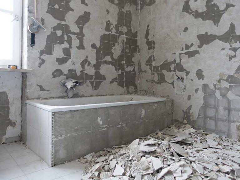 Eine Badewanne steht in einem Zimmer, auf dem Boden ein Haufen mit abgeschlagenen Fliesen
