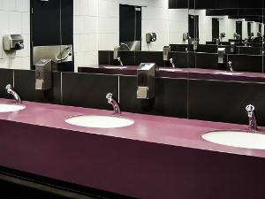Drei Waschbecken nebeneinander mit Seifenspendern an der Wand und einem Spiegel darüber