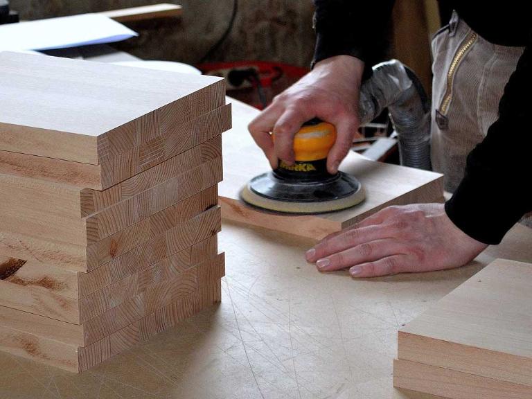 Ein Mensch schleift mit einer Maschine Holzplatten ab