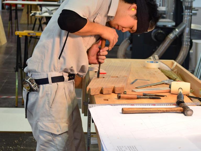 Ein Mensch arbeitet an einem Stück Holz auf einer Werkbank