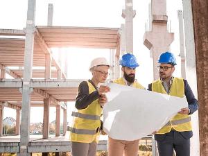 Drei Menschen mit Schutzhelmen und Warnwesten schauen gemeinsam auf einen Bauplan den sie in den Händen halten
