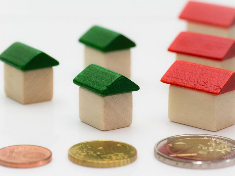 Kleine Häuser aus Holz mit roten und grünen Dächern stehen hinter Geldstücken