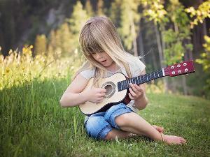 Ein Mädchen sitzt auf einer grünen Wiese und spielt auf einer kleinen Gitarre