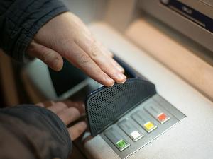 Ein Mensch am Geldautomat gibt seine Geheimzahl ein und hält die Hand über die Tastatur