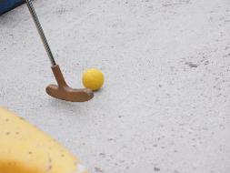 Ein gelber Ball und das Ende eines Minigolfschlägers auf einer Bahn