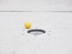 Ein gelber Minigolfball liegt kurz vor dem Loch
