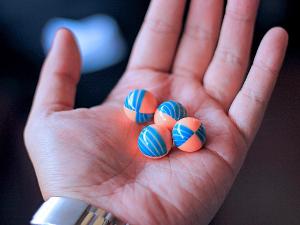 Vier orange-blaue Paintballkugeln liegen in einer Handfläche