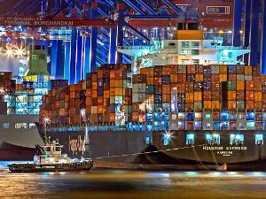 Ein Containerschiff bei Nacht, beleuchtet im Wasser und im Hintergrund Kräne