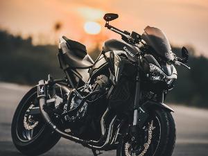 Ein schwarzes Motorrad steht auf einer Straße und im Hintergrund geht die Sonne unter