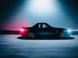 Ein Mensch in einem Auto, Rücklicht rot und vordere Scheinwerfer geben bläuliches Licht ab