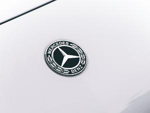 Mercedes Benz Schriftzug um den Mercedesstern herum, auf einer weißlackierten Motorhaube