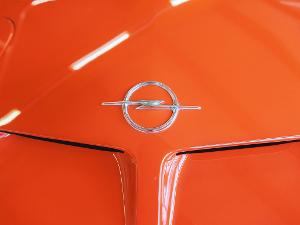 Ein silbernes Opelzeichen auf einer orangefarbenen Motorhaube