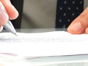 Ein Mensch hält einen Kugelschreiber in der Hand und scheibt etwas auf ein Stück Papier