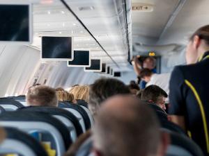 Menschen sitzen in einem Flugzeug auf den Plätzen, eine Stewardess steht im Gang