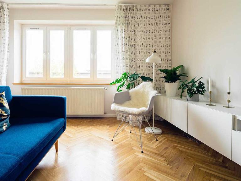 Ein Wohnzimmer mit einem weißen Sideboard, einem Sessel, einer Stehlampe und einem blauen Sofa