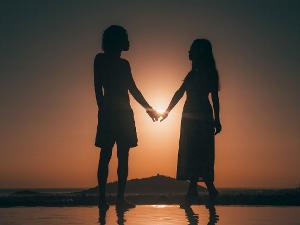 Zwei Menschen halten sich an der Hand vor einem Sonnenuntergang