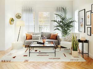 Ein Wohnzimmer mit einem Sofa und darauf platzierten Kissen, einer Stehlampe, Pflanzen, einem Couchtisch auf einem Teppich und Bildern an der Wand