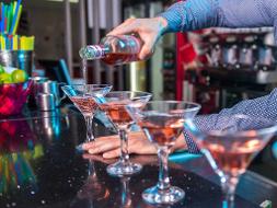 Vier Martinigläser stehen nebeneinander auf dem Tresen und ein Barkeeper befüllt gerade ein Glas