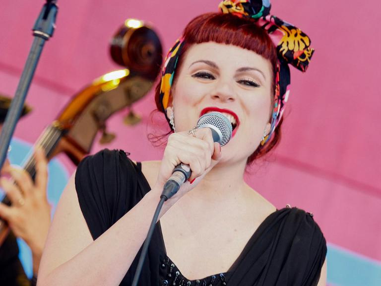 Eine Frau mit roten Haaren und einem Band darin, singt in ein Mikrofon