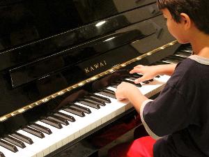 Ein Kind sitzt an einem Kawai Piano, die Hände an den Tasten