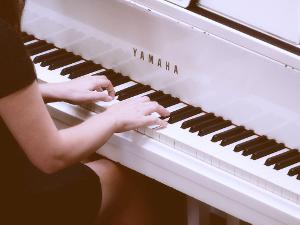 Eine weibliche Person sitzt am und spielt auf einem weißen Klavier