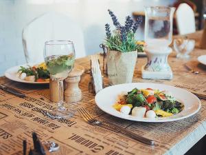 Zwei Teller mit Gemüse stehen auf einem Tisch, mit Gläsern, Salz- und Pfefferstreuer und einem Blümchen gedeckt